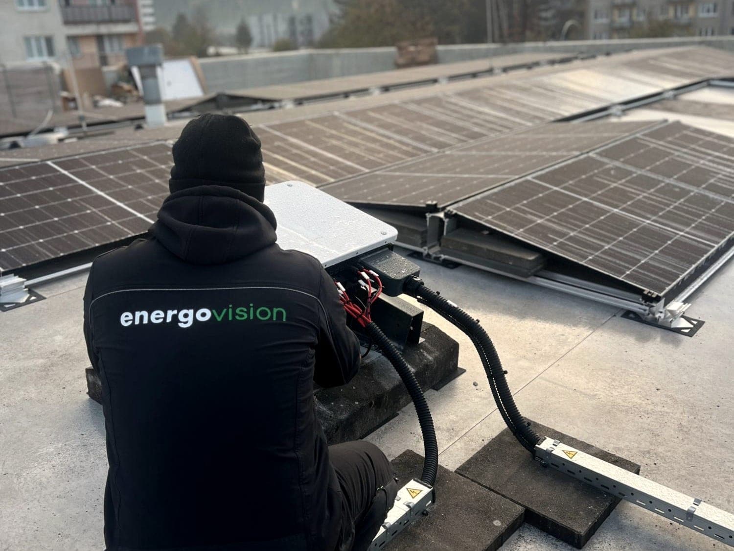 Techniker von Energovision schließt einen Wechselrichter auf dem Flachdach zwischen den Modulreihen an