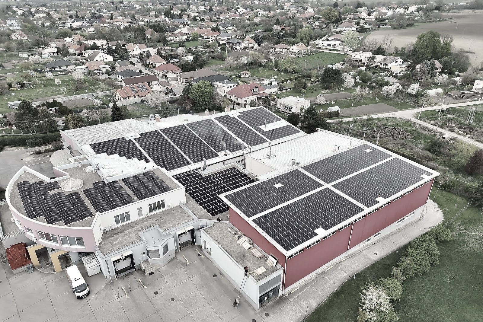 Orthofoto eines Produktionsgeländes mit Photovoltaik auf den Dächern, ringsum Dorf und Felder